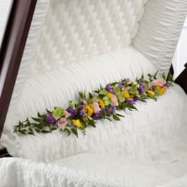 White casket with a colorful floral spray on top
