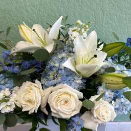 White lilies and roses arranged with blue hydrangeas and small blue flowers
