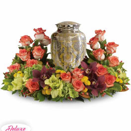 Floral urn arrangement with coral roses and purple orchids around a silver urn