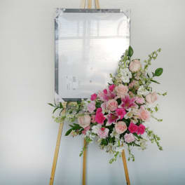 Pink and white floral spray on a wooden easel with a framed sign