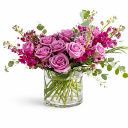 Pink roses and magenta flowers arranged in a clear glass vase