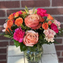 Bouquet of peach and orange roses with pink carnations in a glass vase