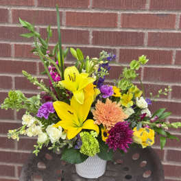 Mixed bouquet with yellow lilies, purple blooms, and a white vase