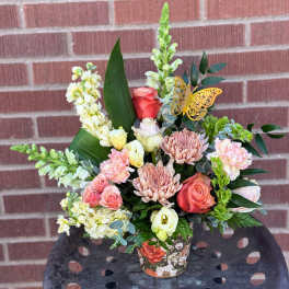 Mixed bouquet in a floral-patterned container with pink and cream flowers