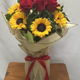 Bouquet of red roses and yellow sunflowers wrapped in tan paper with a red ribbon