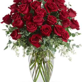 Tall arrangement of long-stemmed red roses in a clear glass vase with filler