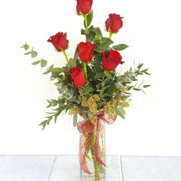 Tall bouquet of red roses in a clear glass vase with ribbon