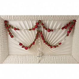 Red rosebud rosary draped across a white pleated casket interior.