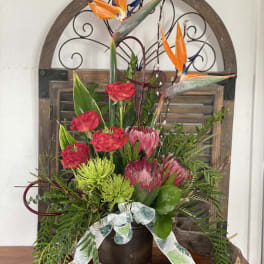 Tall floral arrangement with orange bird-of-paradise and red blooms in a dark vase