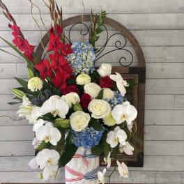Tall floral arrangement with red gladiolus, white orchids, and blue hydrangeas in a white vase