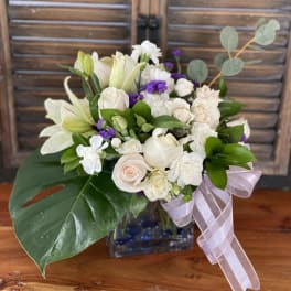 White roses and lilies in a glass vase with a lavender ribbon