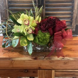 Red roses and green orchids in a glass vase with a red ribbon