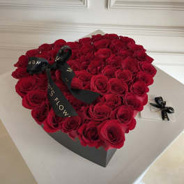 Heart-shaped box filled with red roses and a black ribbon