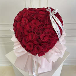 Heart-shaped bouquet of red roses with pale pink wrapping and white ribbon