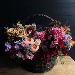 Basket arrangement of roses, orchids, and hydrangeas in deep pink and burgundy tones