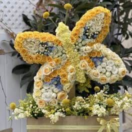 Butterfly-shaped floral arrangement of yellow and white roses with blue accents