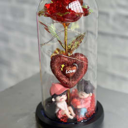 Red decorative rose under a clear dome with two small figurines at the base