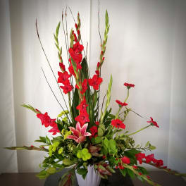 Tall floral arrangement with red gladiolus, pink lily, and green chrysanthemums in a white vase