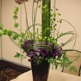 Tall purple and green floral arrangement in a black vase