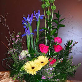 Mixed bouquet with pink roses, yellow gerberas, and purple irises in a green vase