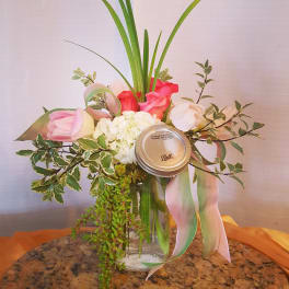 Pink and white floral arrangement in a glass jar with a ribbon and mason jar lid