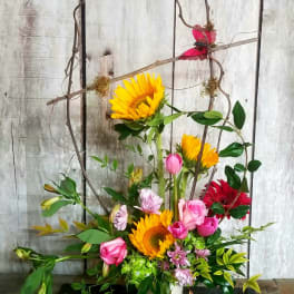 Tall mixed bouquet with sunflowers, pink roses, and gerbera daisies in a white vase