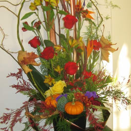 Tall autumn floral arrangement with roses and small pumpkins in a black container