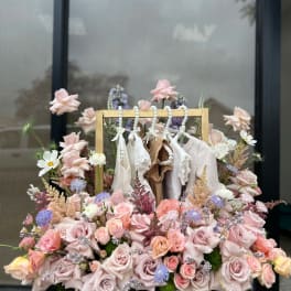 Pastel rose arrangement with hanging baby clothes in a wooden frame