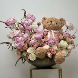 Pink and white flower arrangement with a teddy bear in a bowl vase