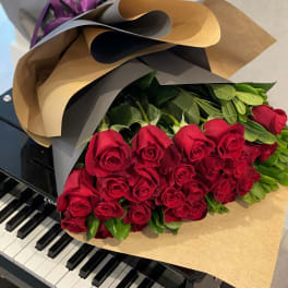 Bouquet of long-stem red roses wrapped in kraft paper resting on a black piano keyboard