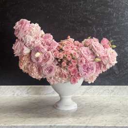Pink rose arrangement in a white pedestal vase
