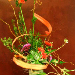 Tall floral arrangement with orange blooms in a square vase