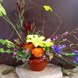 Colorful floral arrangement in a red vase with lilies, roses, and orchids