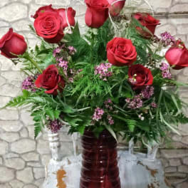 Tall arrangement of red roses with small pink blossoms in a red glass vase