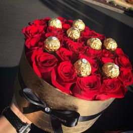 Round box of red roses topped with gold-wrapped chocolates
