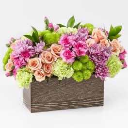 Mixed pink and peach flowers arranged in a rectangular wooden box