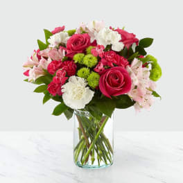 Arrangement of pink roses, white carnations, green button mums, and pink alstroemeria in a clear glass vase