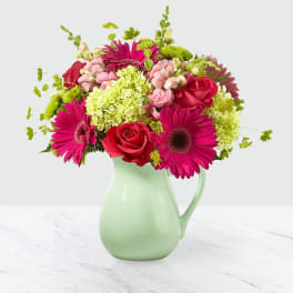 Pink and red flowers arranged in a pale green pitcher vase