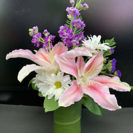 Pink lilies and white daisies in a green vase with purple flowers
