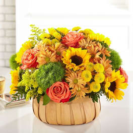 Basket arrangement of sunflowers, roses, and mums in yellow and orange tones