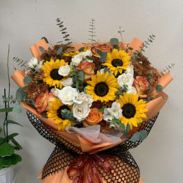 Bouquet of sunflowers, roses, and white blooms wrapped in orange paper