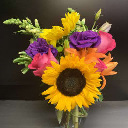 Bright mixed bouquet with sunflowers, roses, and lilies in a glass vase