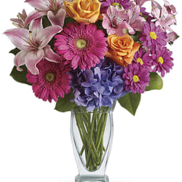 Mixed bouquet of pink, purple, and orange flowers in a clear glass vase