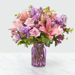 Pink lilies and roses arranged in a purple glass vase