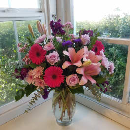 Mixed bouquet of pink lilies, roses, and gerbera daisies in a glass vase