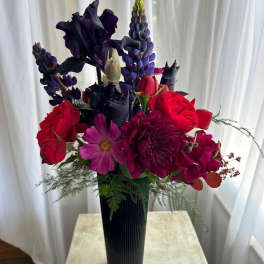 Tall bouquet of red and purple flowers in a black vase