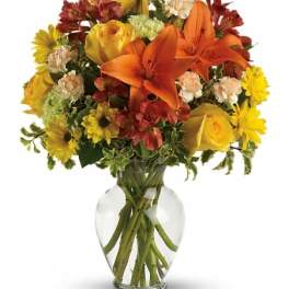 Bouquet of orange lilies, yellow roses, and mixed flowers in a clear glass vase