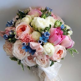 Round bouquet of pink, white, and blue flowers with lace ribbon
