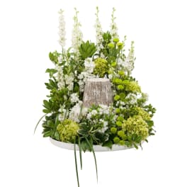 Woodland-style arrangement of white and green flowers around a rustic tree-stump accent on a white tray