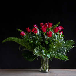 Arrangement of long-stemmed red roses with abundant foliage in a clear glass vase